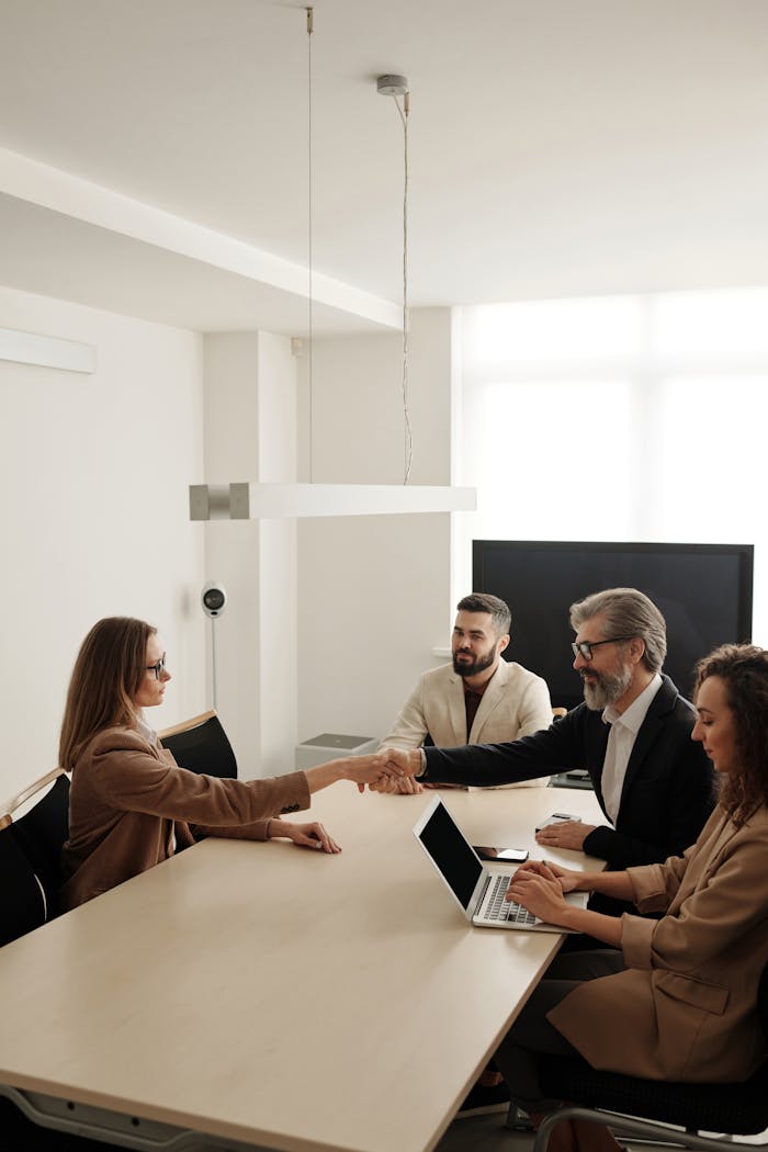 gallery-2 Business professionals engaging in a handshake across a conference table, signifying successful collaboration.